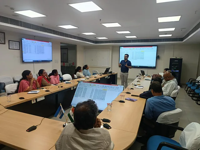 Participants listening to a presenter in a boardroom with wall-mounted screens