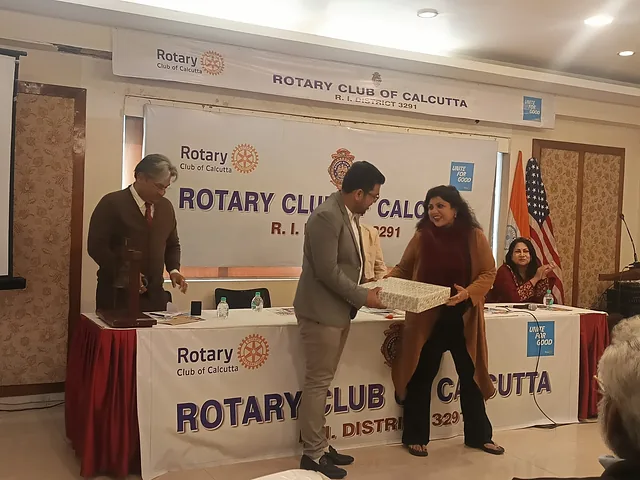 Presenter and a guest holding a gift box in front of an event banner