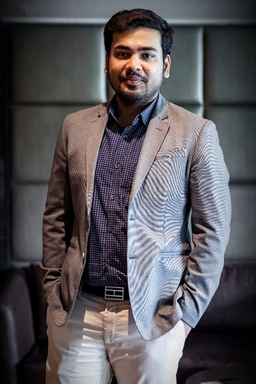 Aveek Agarwal in a grey blazer and patterned shirt, standing with his hands in his pockets